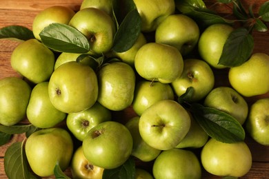 Photo of Ripe green apples with leaves on wooden table, flat lay