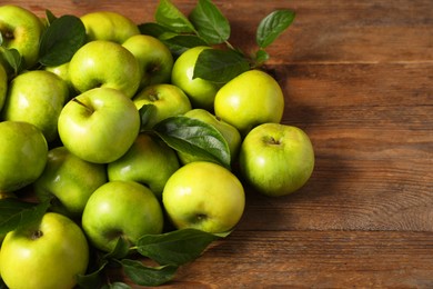 Photo of Ripe green apples with leaves on wooden table. Space for text