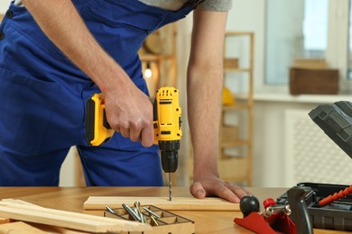 Photo of Craftsman working with drill at wooden table in workshop, closeup