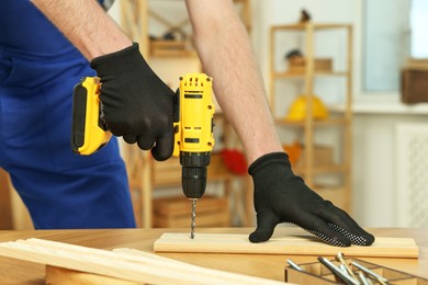 Photo of Craftsman working with drill at wooden table in workshop, closeup