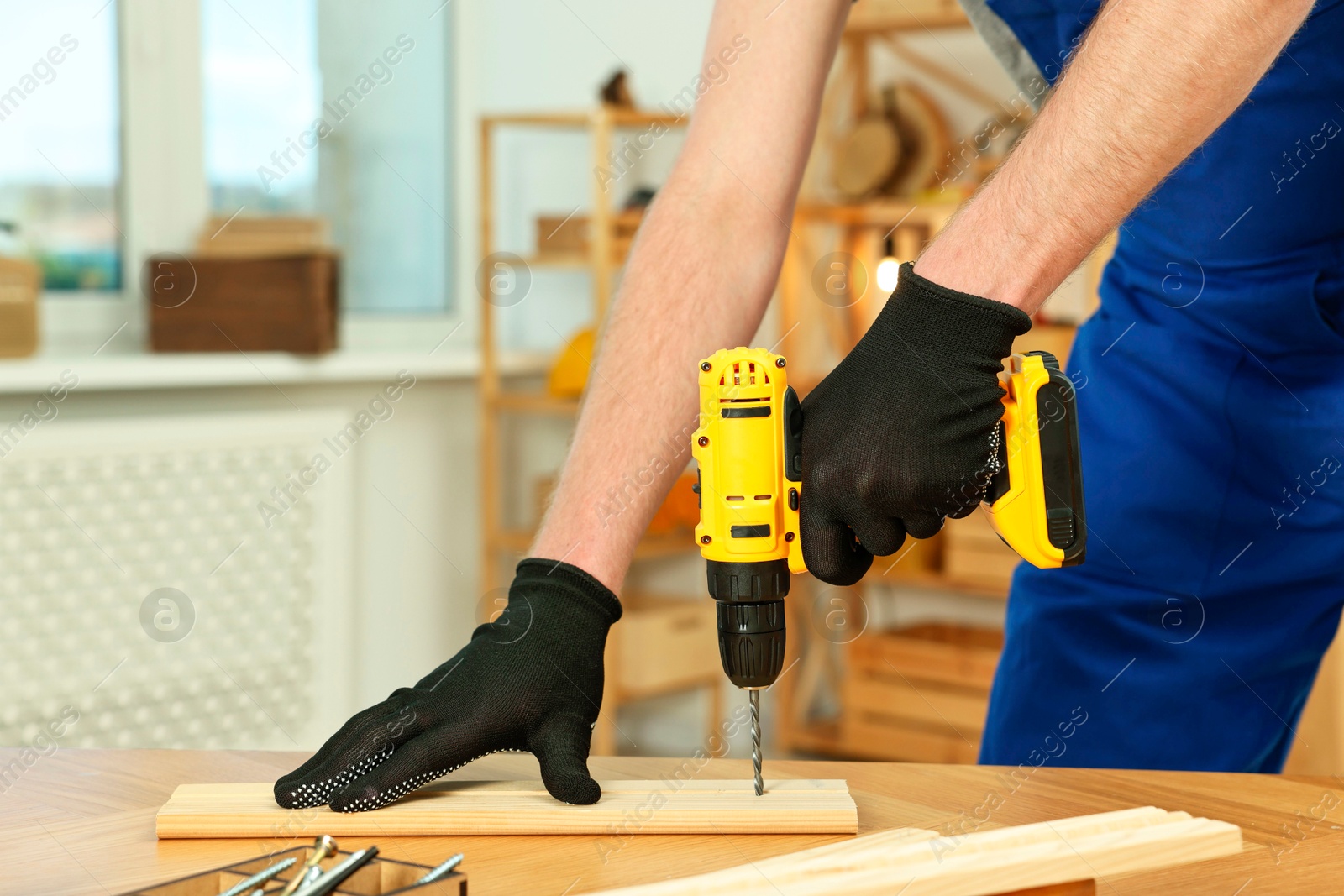 Photo of Craftsman working with drill at wooden table in workshop, closeup