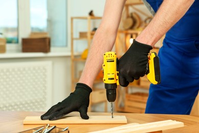 Photo of Craftsman working with drill at wooden table in workshop, closeup