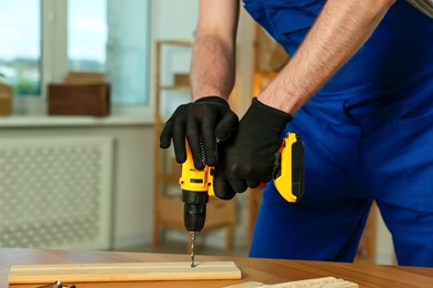 Craftsman working with drill at wooden table in workshop, closeup. Space for text