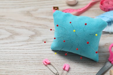 Photo of Light blue pincushion with pins and other sewing tools on wooden table, closeup. Space for text