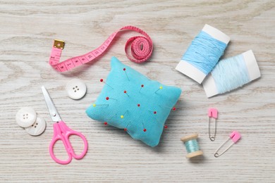 Photo of Light blue pincushion with pins and other sewing tools on wooden table, flat lay