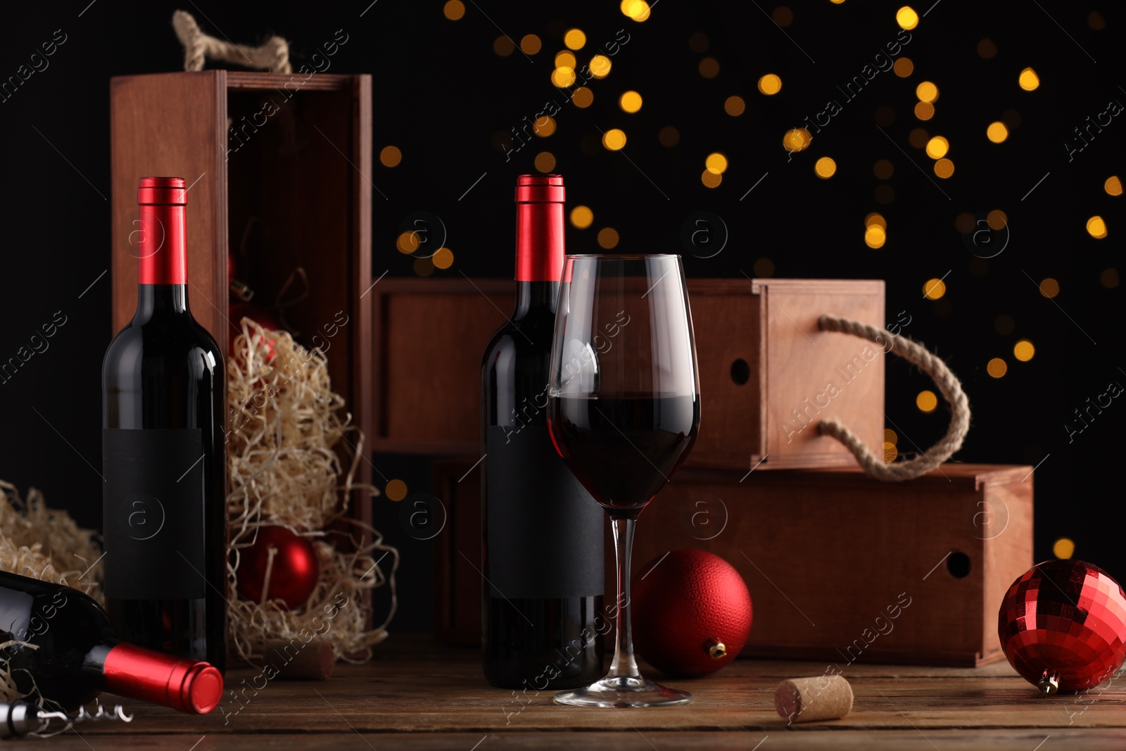 Photo of Bottles of wine, glass, wooden boxes, corkscrew and red Christmas balls on table