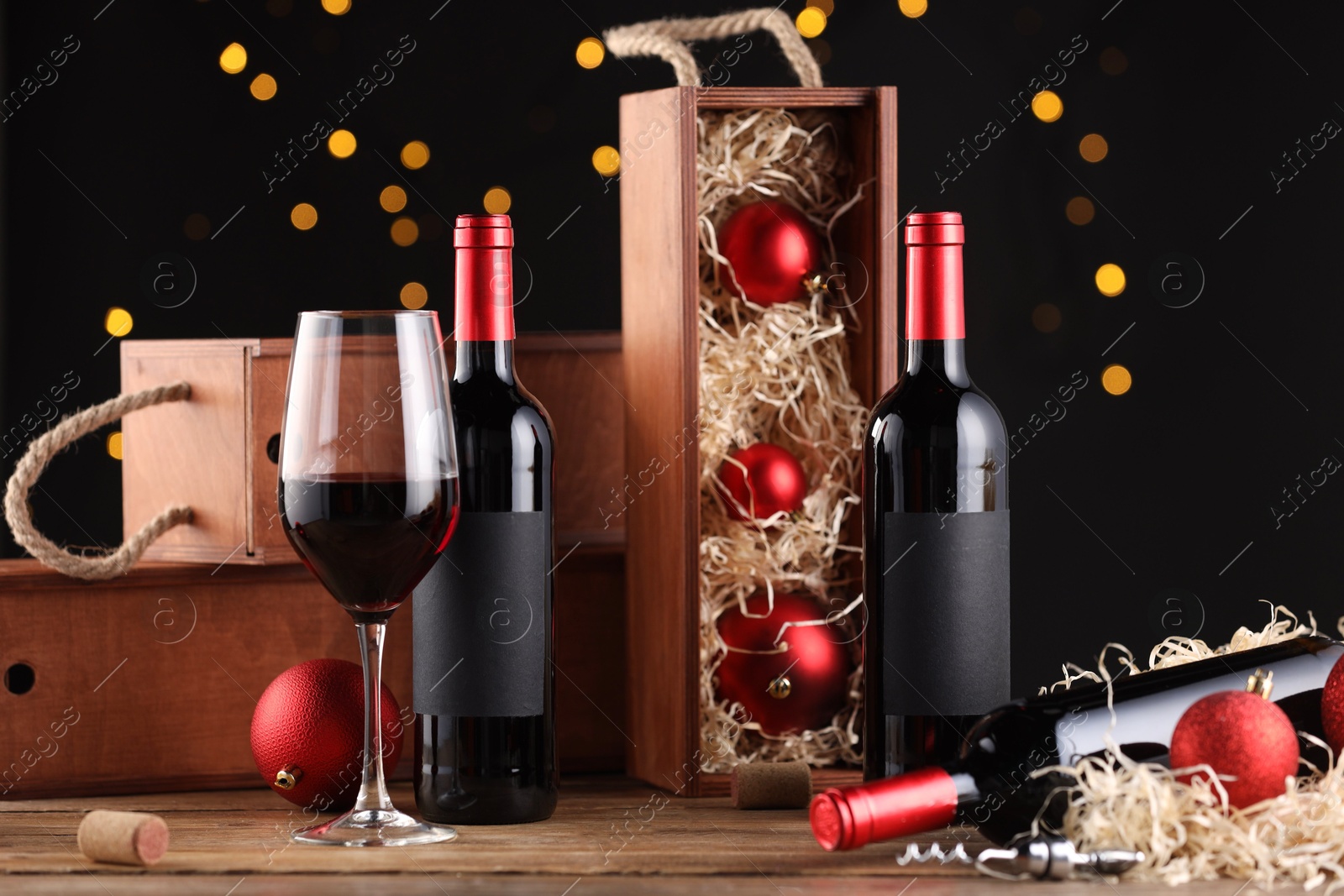 Photo of Bottles of wine, glass, wooden boxes, corkscrew and red Christmas balls on table