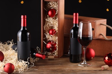 Photo of Bottles of wine, glass, wooden boxes, corks and red Christmas balls on table