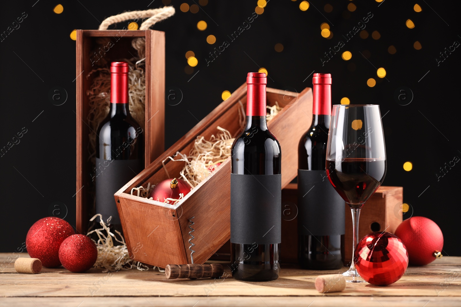 Photo of Bottles of wine, glass, wooden boxes, corks and red Christmas balls on table