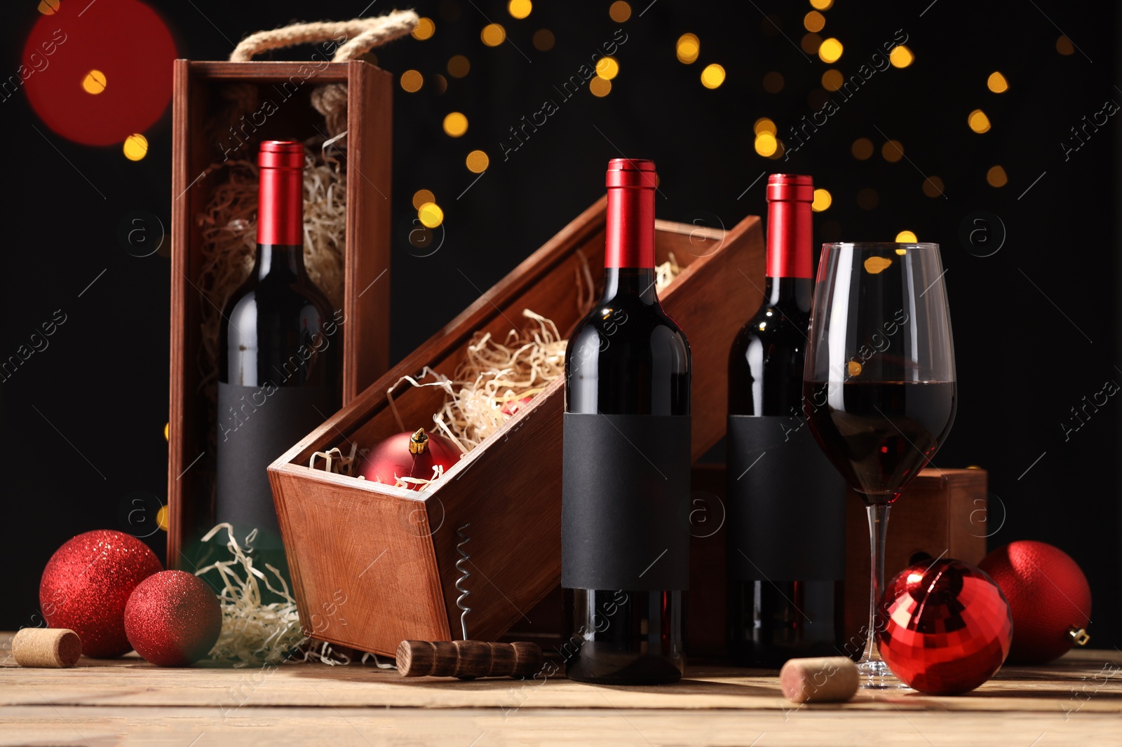 Photo of Bottles of wine, glass, wooden boxes, corks and red Christmas balls on table