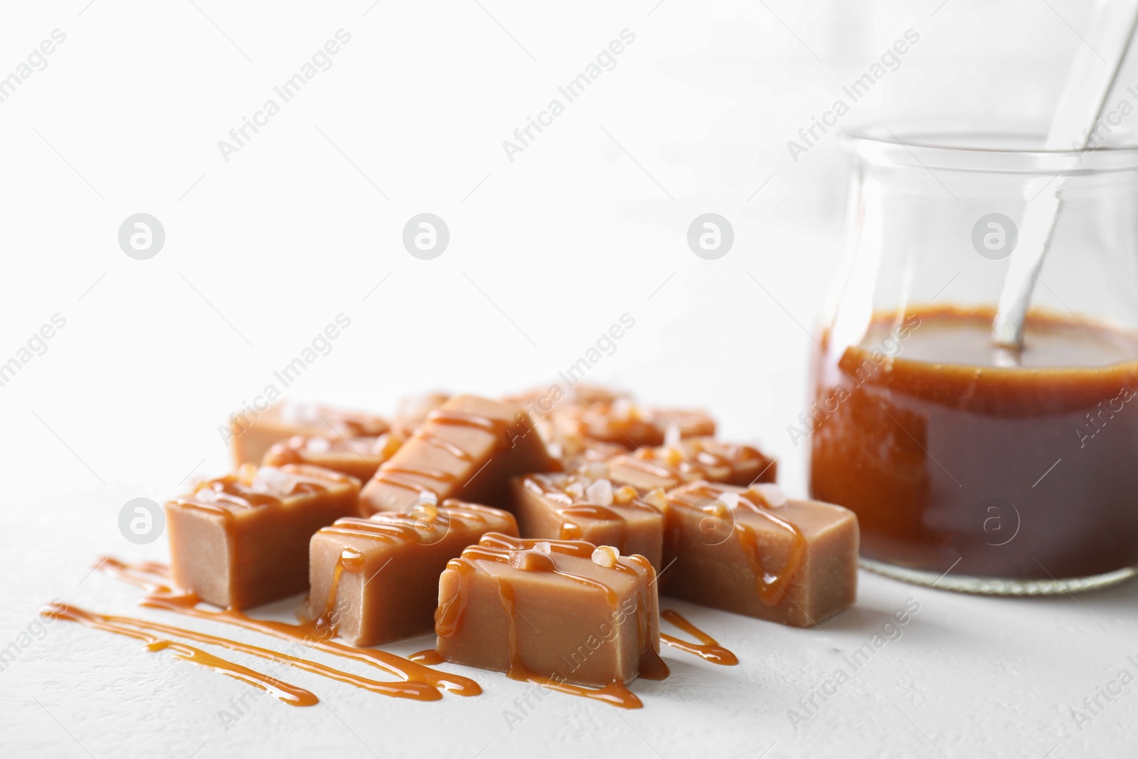 Photo of Tasty candies, caramel sauce and salt on white table