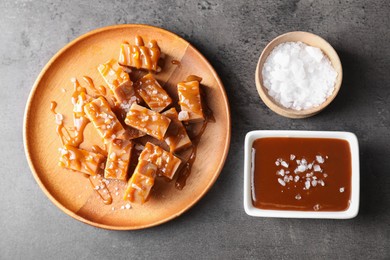 Photo of Plate with tasty candies, caramel sauce and salt on grey table, top view