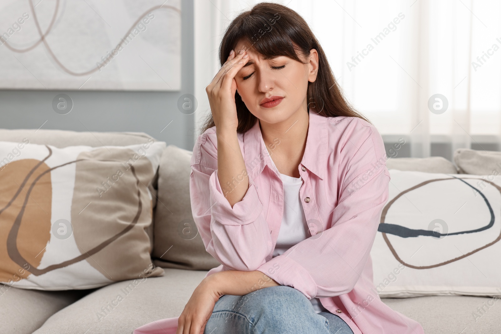 Photo of Upset woman suffering from headache on sofa at home