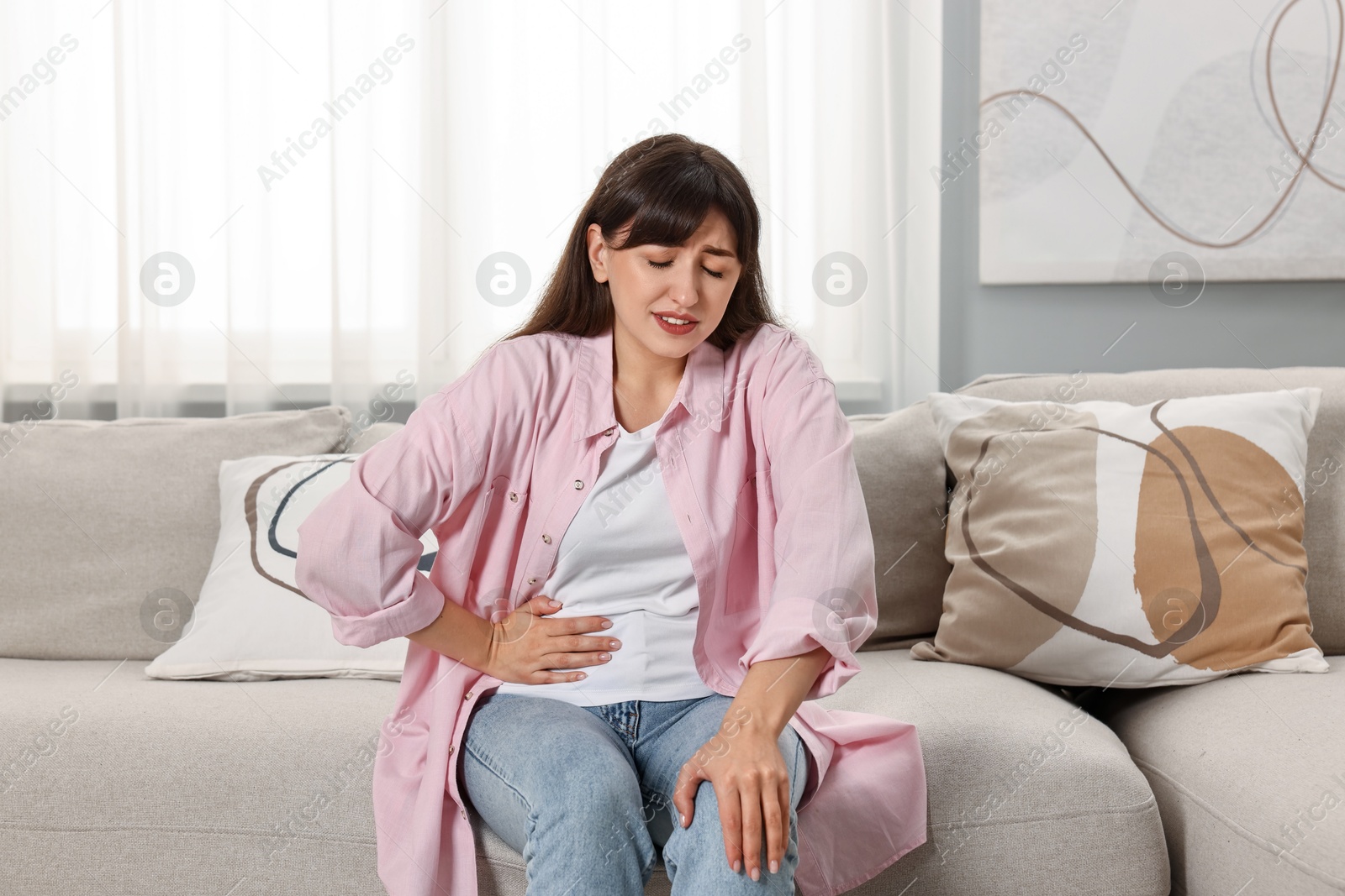 Photo of Upset woman suffering from abdominal pain on sofa at home