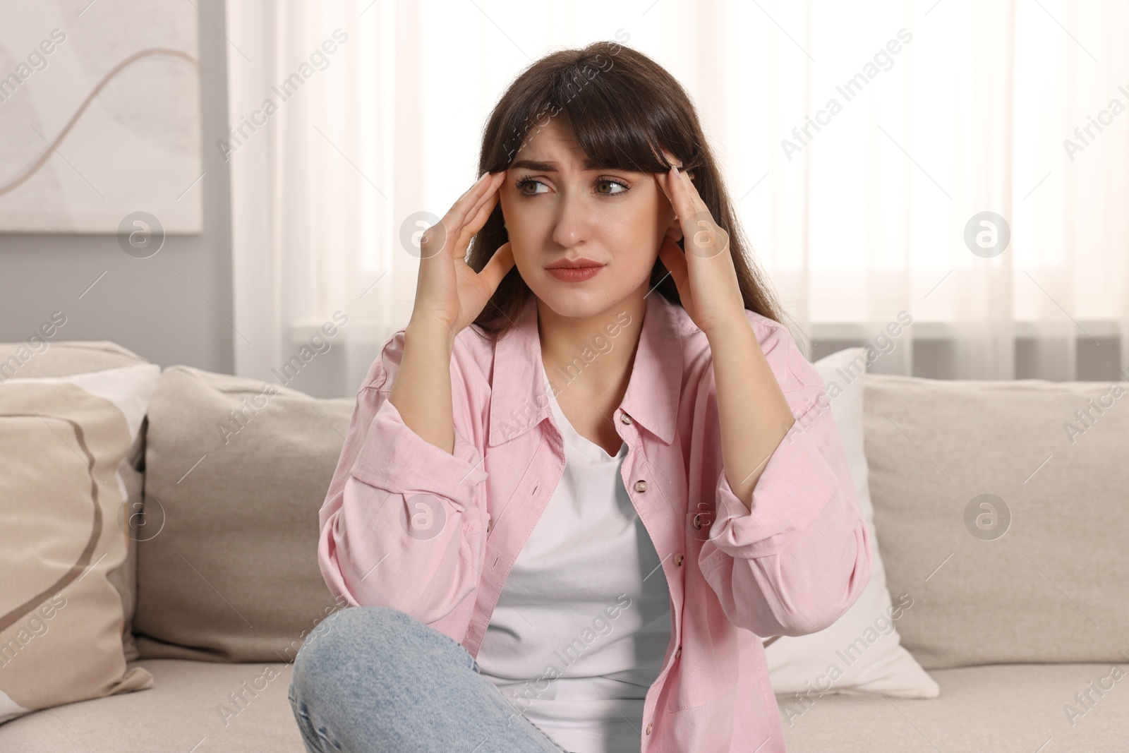 Photo of Upset woman suffering from headache on sofa at home