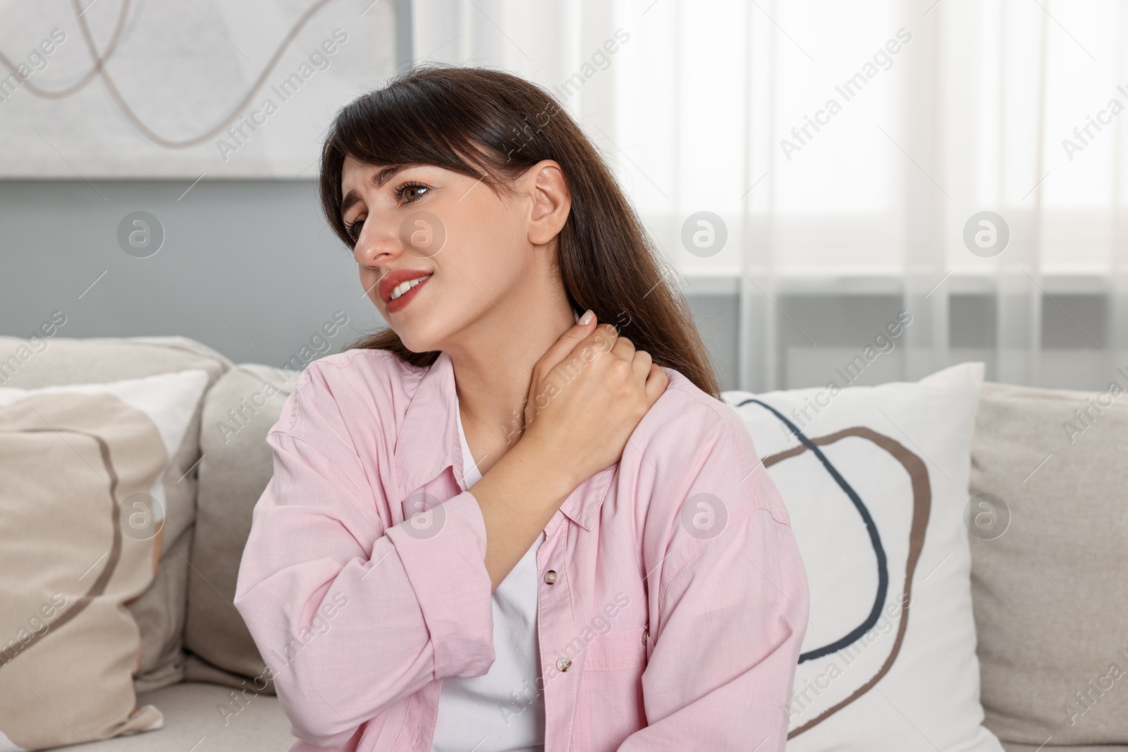 Photo of Upset woman suffering from neck pain on sofa at home