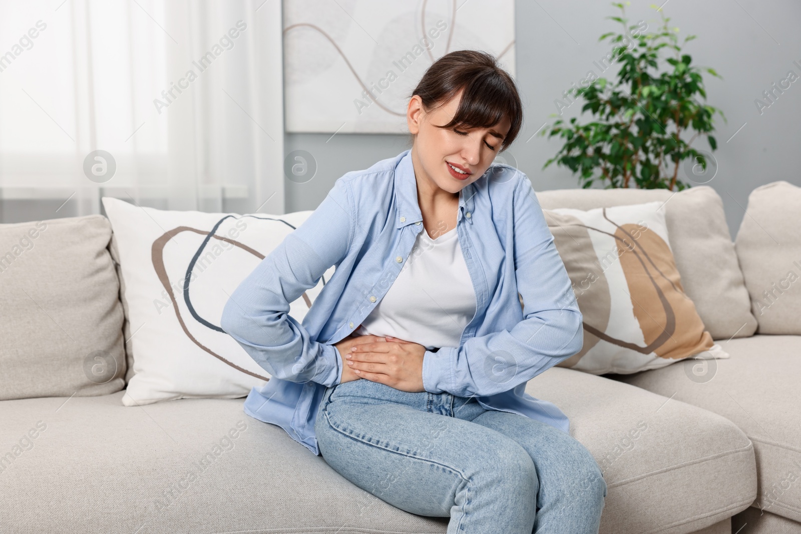 Photo of Upset woman suffering from abdominal pain on sofa at home