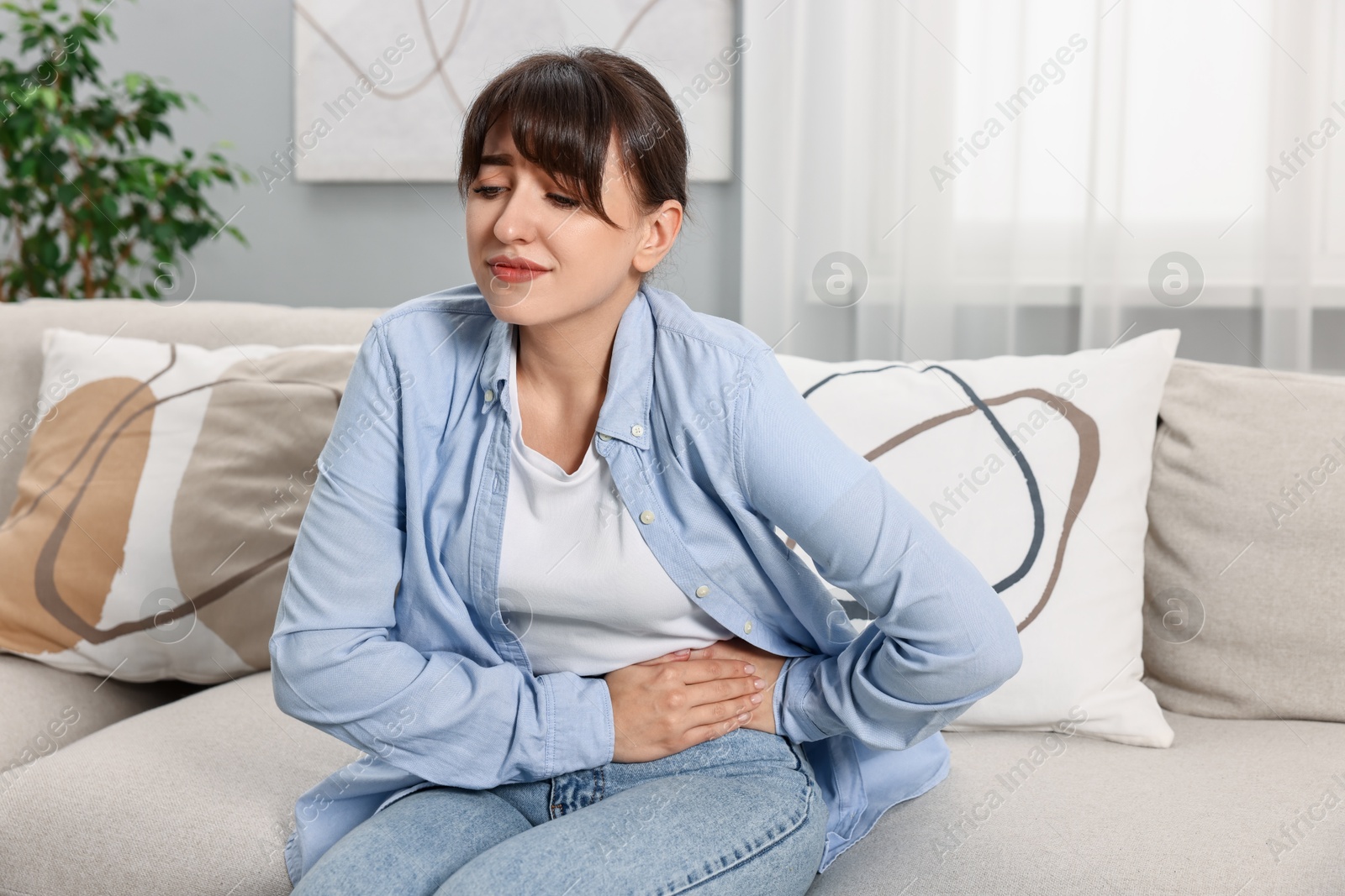 Photo of Upset woman suffering from abdominal pain on sofa at home