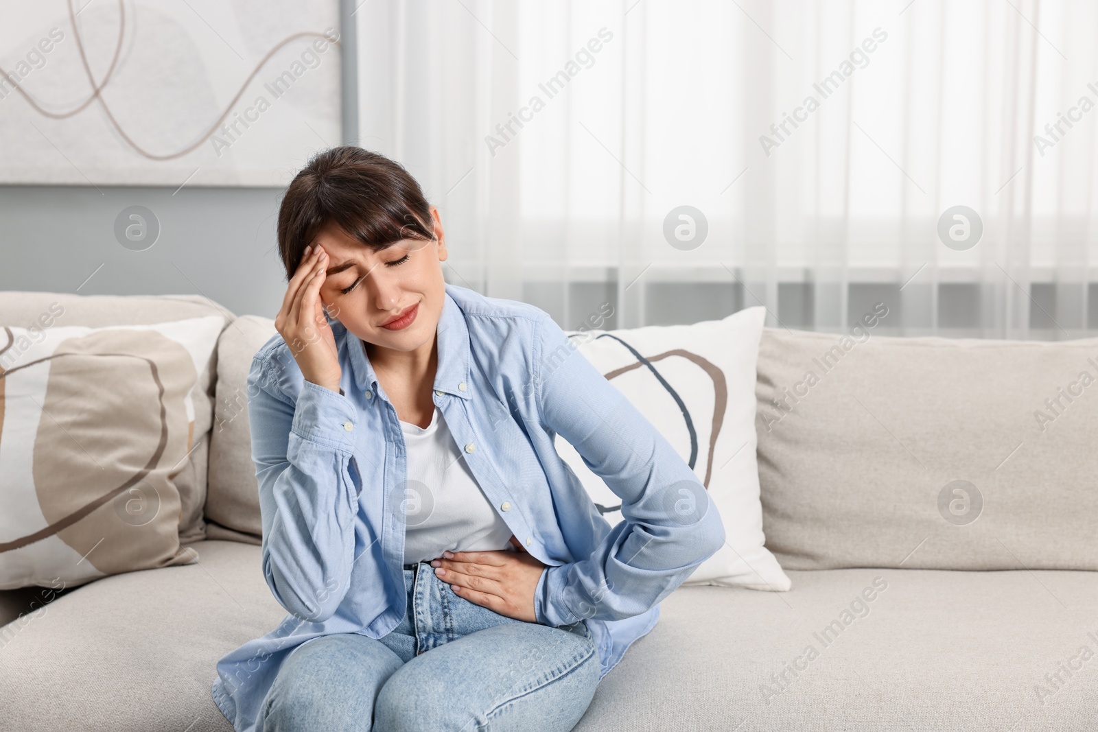 Photo of Upset woman suffering from headache on sofa at home