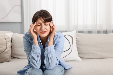 Photo of Upset woman suffering from headache on sofa at home