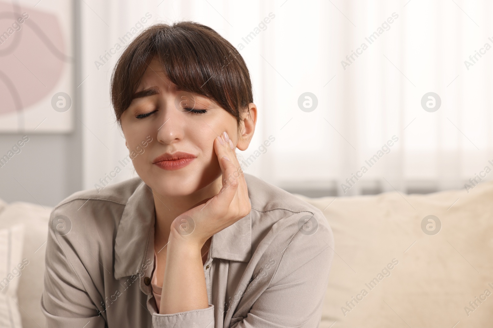 Photo of Upset young woman suffering from toothache indoors, space for text