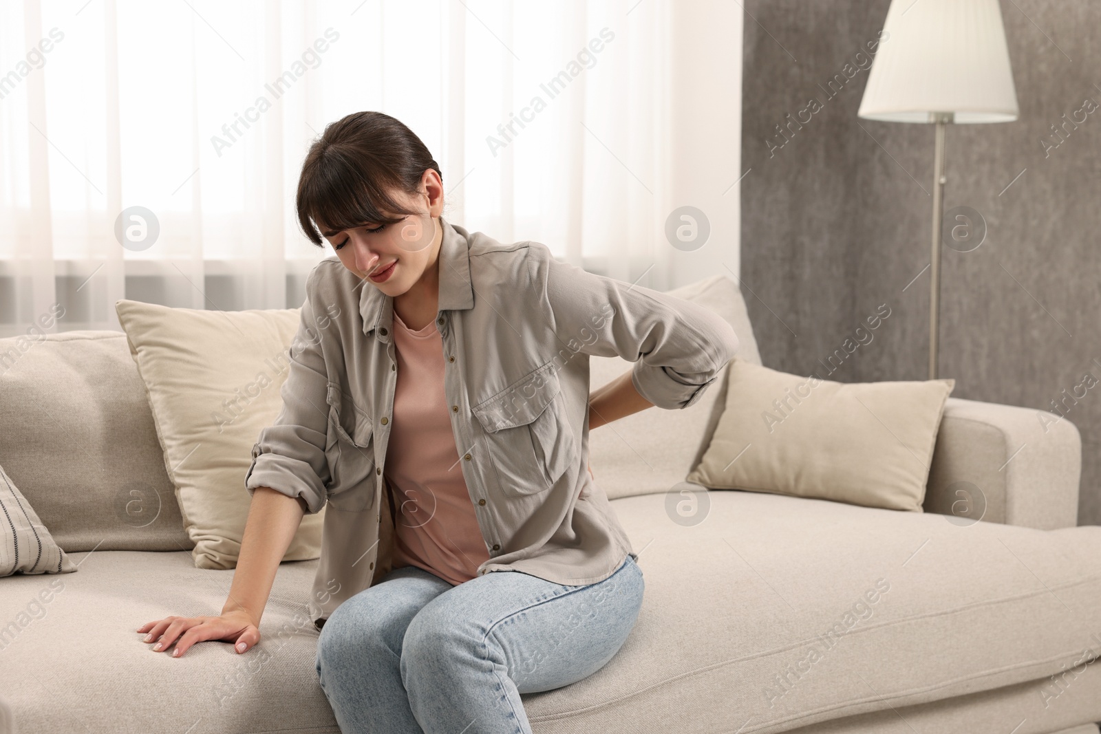 Photo of Upset woman suffering from back pain on sofa at home