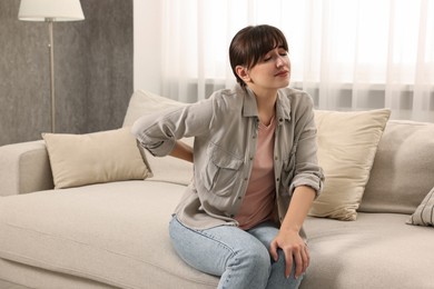 Photo of Upset woman suffering from back pain on sofa at home