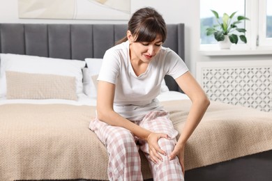 Photo of Upset woman suffering from knee pain on bed at home