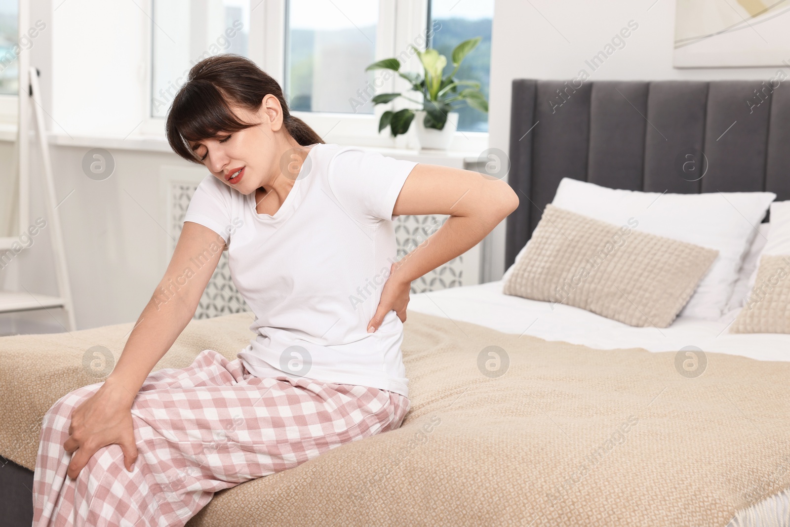 Photo of Upset woman suffering from back pain on bed at home