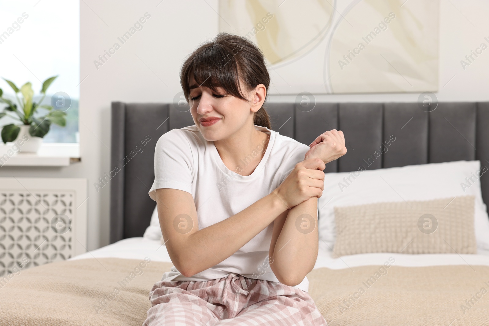 Photo of Upset woman suffering from pain in wrist on bed at home