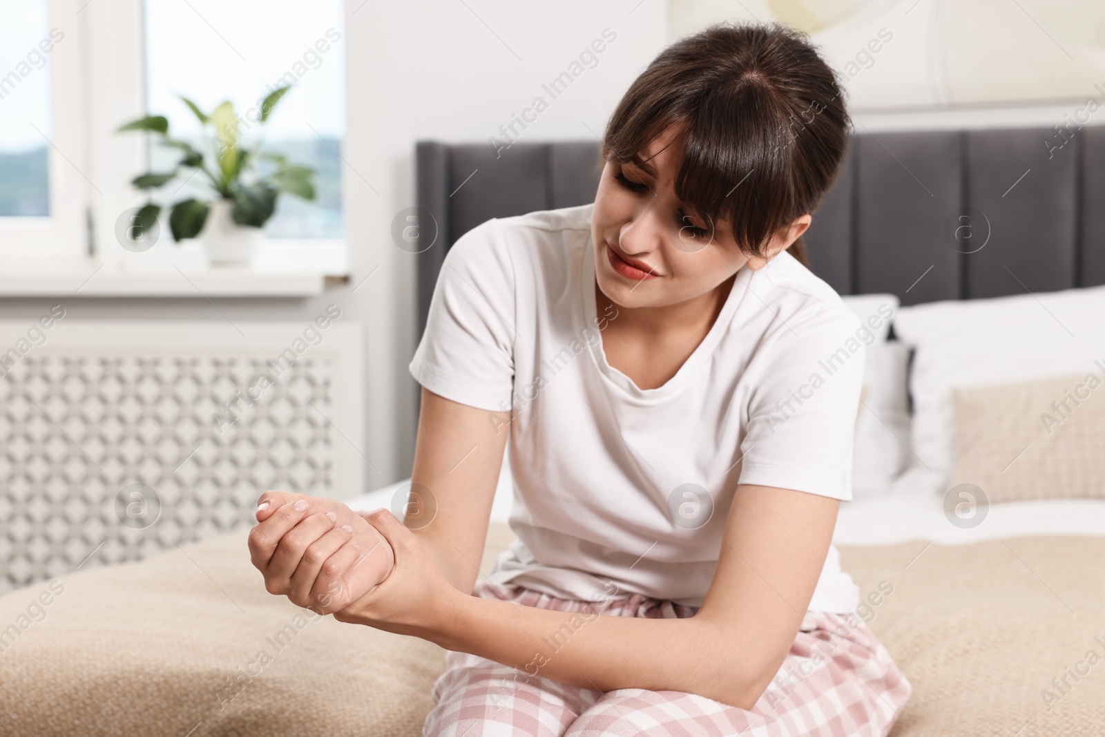 Photo of Upset woman suffering from pain in wrist on bed at home