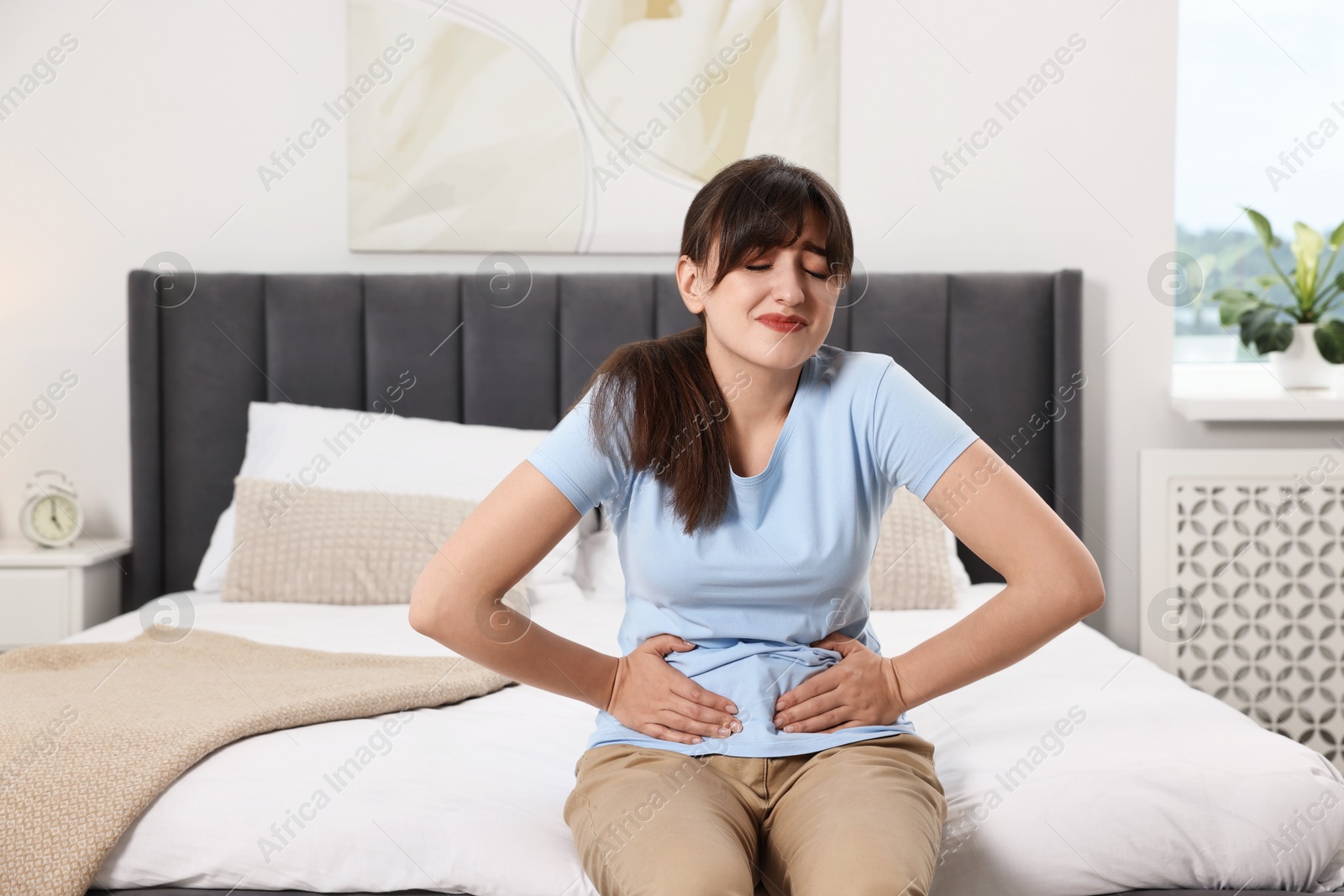 Photo of Upset woman suffering from abdominal pain on bed at home