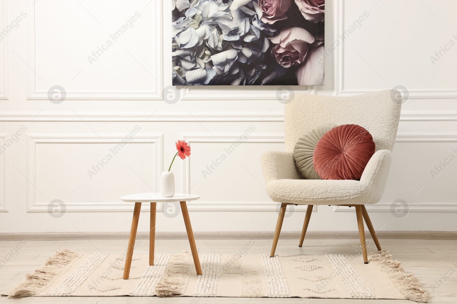 Photo of Soft armchair, coffee table with flower and picture in stylish room