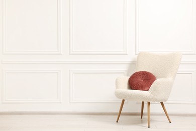 Soft armchair with pillow in light room. Space for text