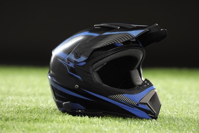 Photo of Modern motorcycle helmet with visor on green grass against black background