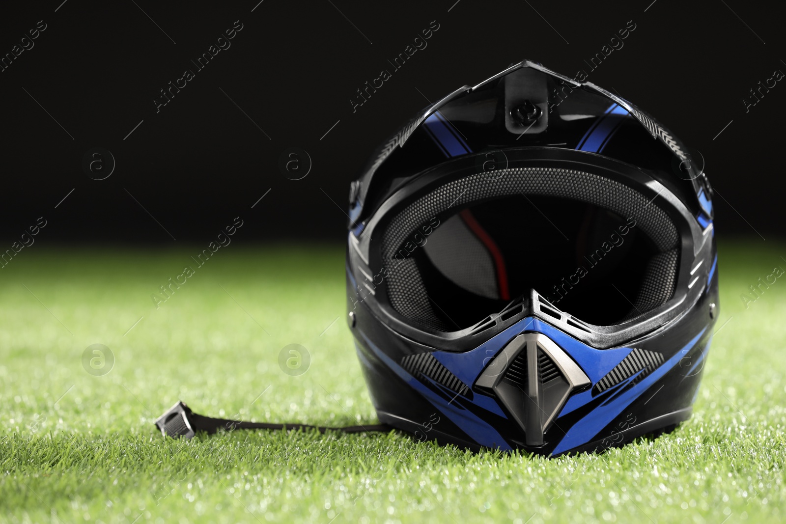 Photo of Modern motorcycle helmet with visor on green grass against black background, space for text