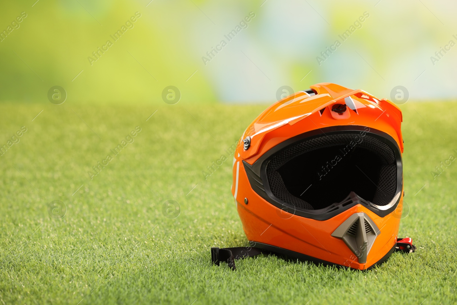 Photo of Orange motorcycle helmet with visor on green grass, space for text