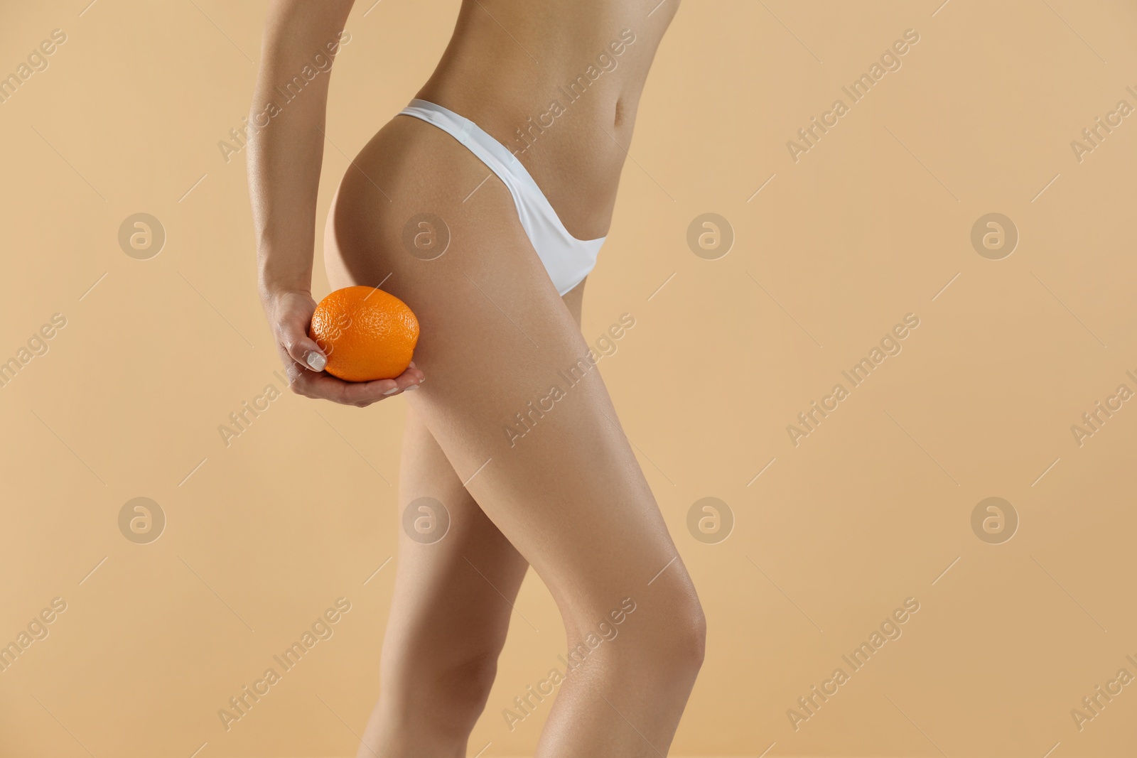 Photo of Woman in underwear with orange on beige background, closeup. Cellulite problem