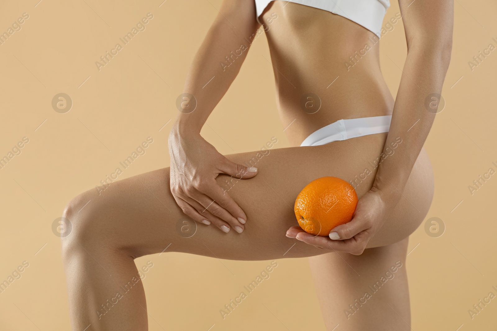 Photo of Woman in underwear with orange on beige background, closeup. Cellulite problem