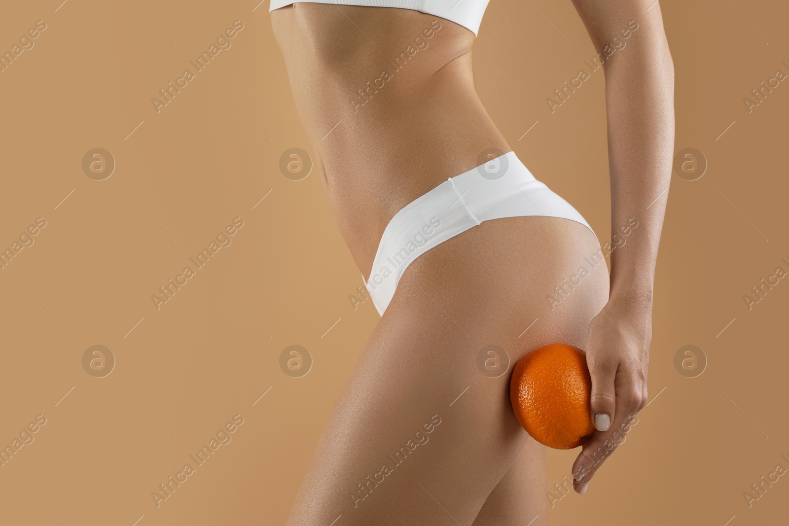 Photo of Woman in underwear with orange on beige background, closeup. Cellulite problem