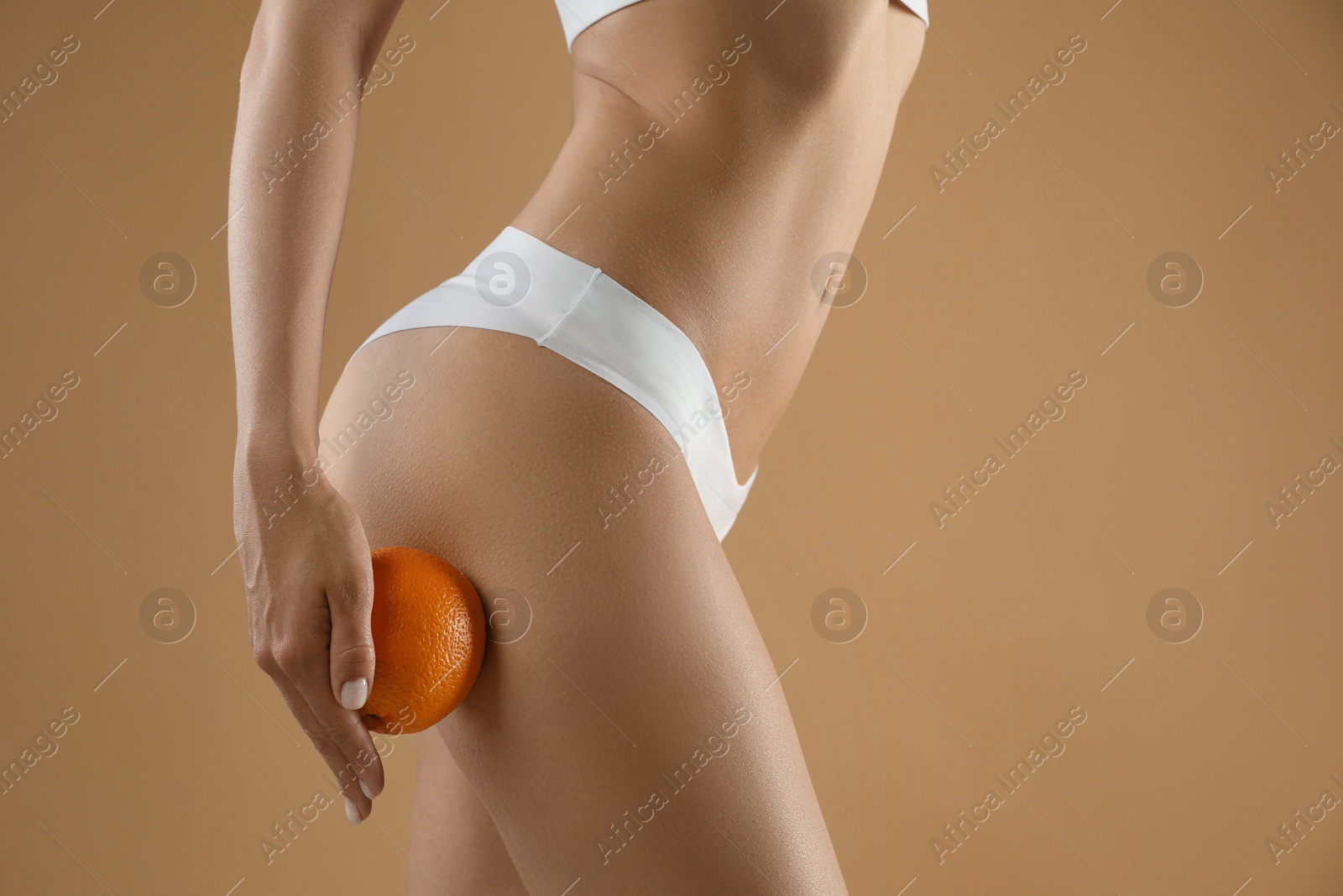 Photo of Woman in underwear with orange on beige background, closeup. Cellulite problem