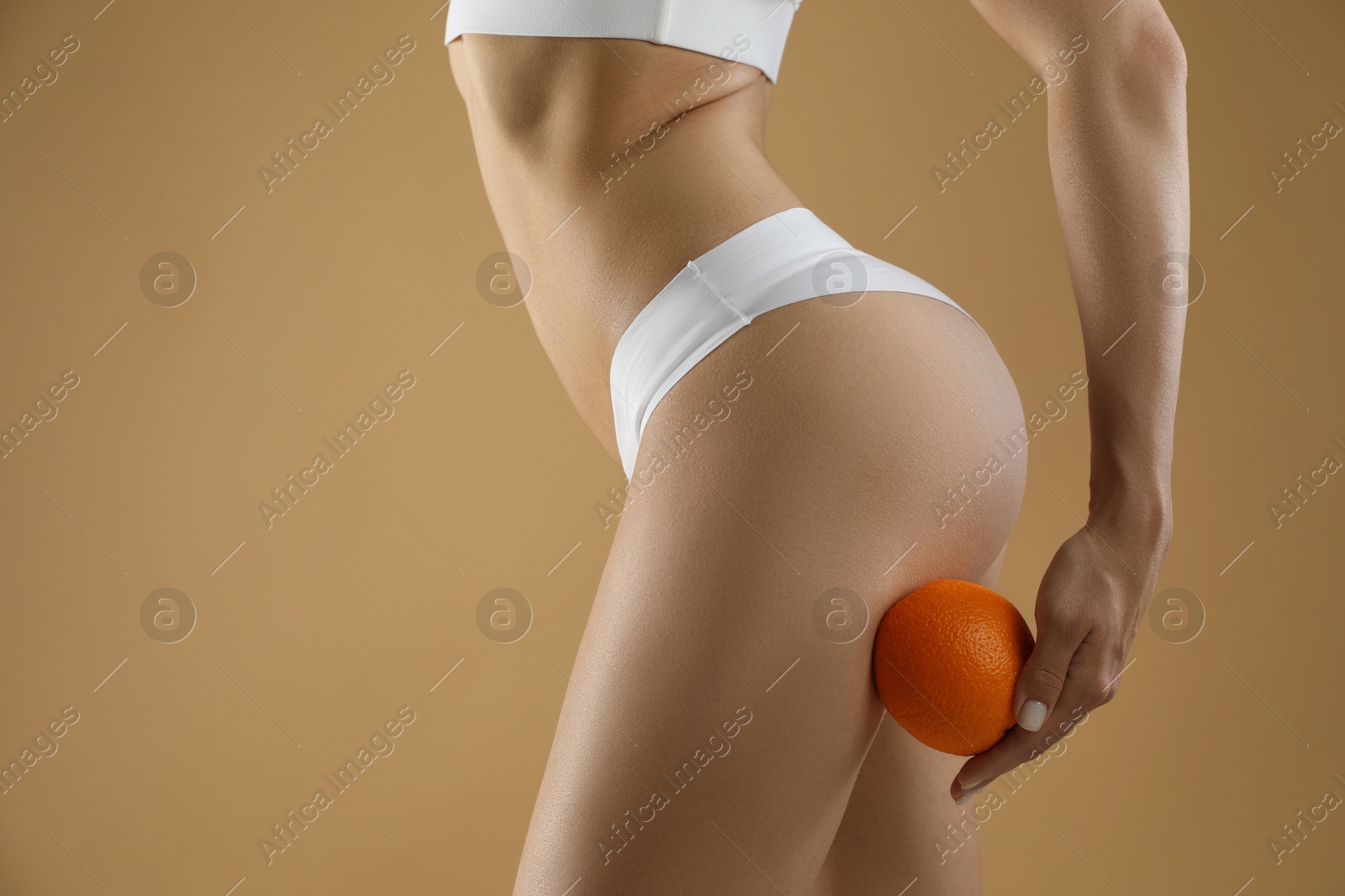 Photo of Woman in underwear with orange on beige background, closeup. Cellulite problem