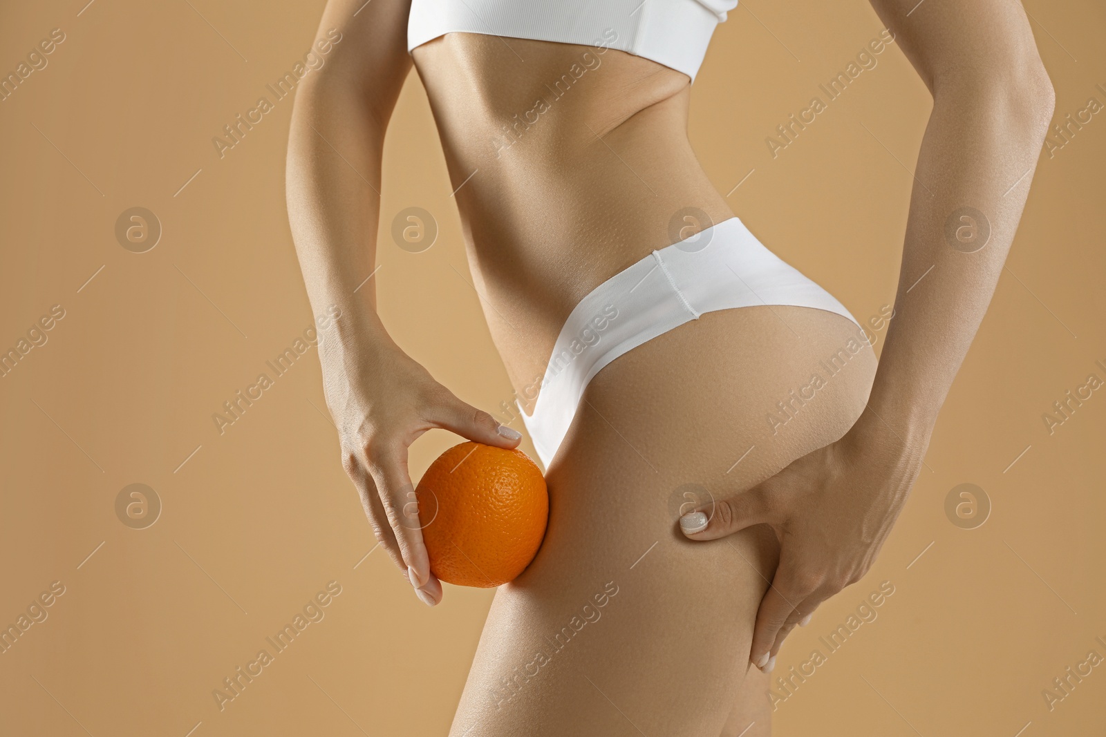 Photo of Woman in underwear with orange on beige background, closeup. Cellulite problem