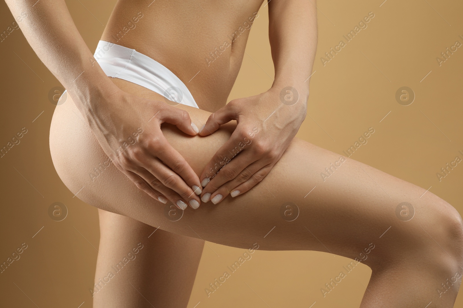 Photo of Woman in underwear making heart with hands near thigh on beige background, closeup. Cellulite problem