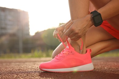 Photo of Woman tying shoelace of pink sneaker at stadium, closeup. Space for text