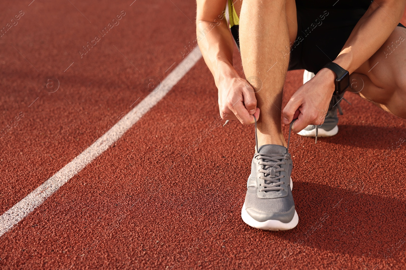 Photo of Man tying shoelace of grey sneaker at stadium, closeup. Space for text