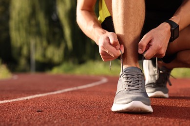 Photo of Man tying shoelace of grey sneaker at stadium, closeup. Space for text