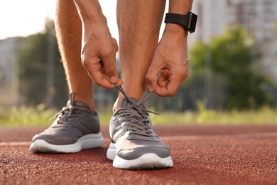 Photo of Man tying shoelace of grey sneaker at stadium, closeup