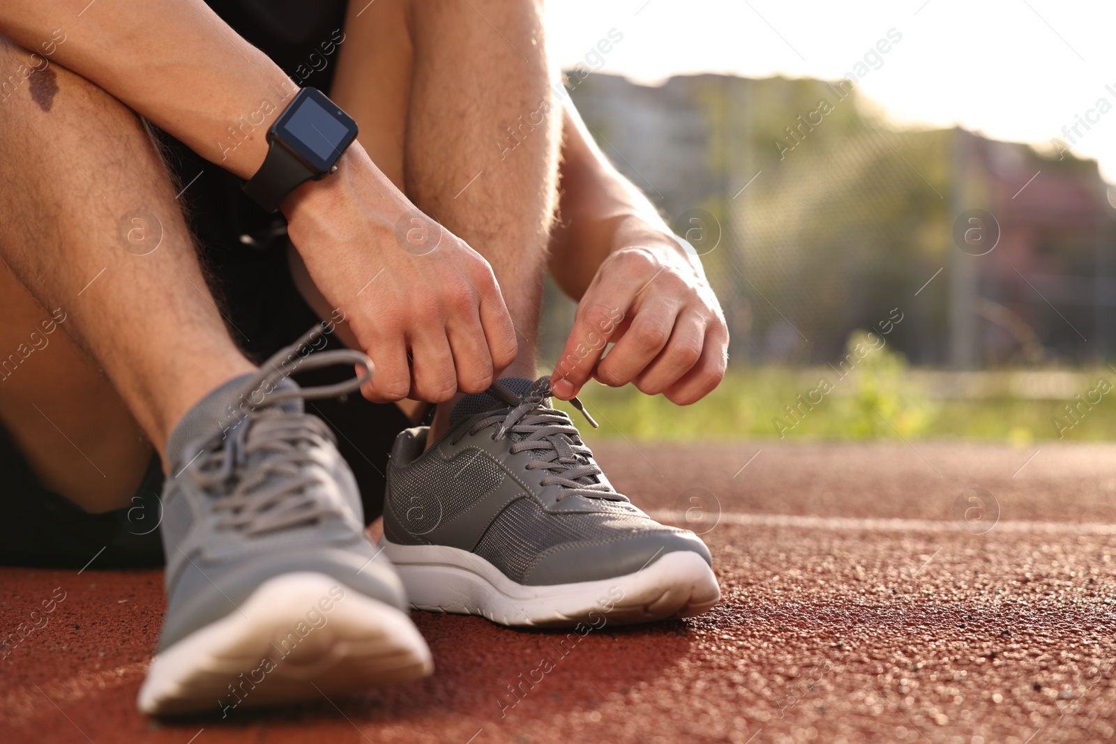 Photo of Man tying shoelace of grey sneaker at stadium, closeup. Space for text