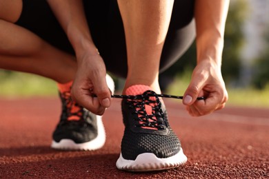 Woman tying shoelace of sneaker at stadium, closeup